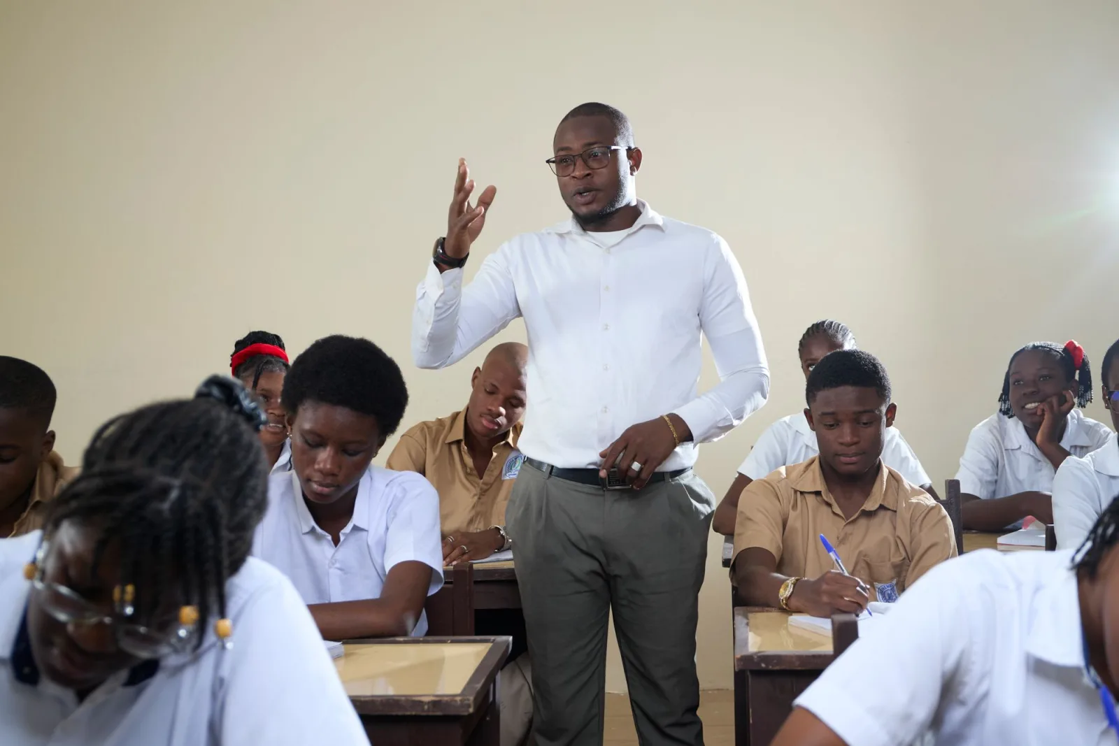 A teacher standing among secondary school students, explaining a lesson. Photo by Mickael Ange Konan on Pexels.